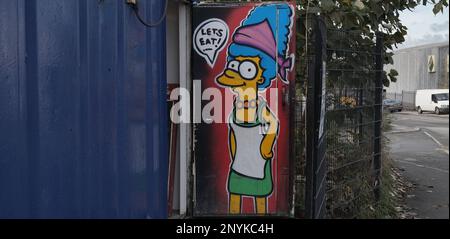 Industriegebiete sind nicht für jedermann, aber es gibt viel zu sehen, wenn man sich umsieht. Wie immer, da es ein guter Weg zu allen Geschäften ist, haben Caterer eine Nische entdeckt und es waren mindestens zwei hier, die die zahlreichen kleinen Fabriken und Geschäfte bedienen. Diese befindet sich in einem recycelten Versandcontainer, der während der Öffnungszeiten plötzlich eine hell bemalte Tür enthüllt, die mit dem beliebten Simpsons-Charakter aller dekoriert ist. Ich bin sicher, Matt Groening würde es gutheißen! Fox würde wahrscheinlich klagen, also werde ich den Ort nicht verraten. Stockfoto