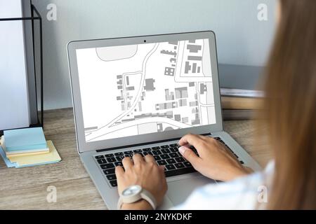 Frau analysiert Katasterkarte auf Laptop am Tisch, Nahaufnahme Stockfoto