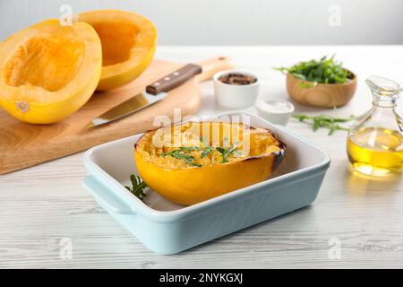 Die Hälfte des gekochten Spaghetti-Kürbiss mit Rucola in einer Backform auf einem weißen Holztisch Stockfoto