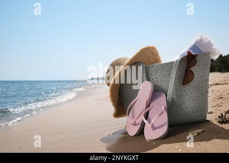 Tasche mit Strandaccessoires und Flip-Flops am Meer. Platz für Text Stockfoto