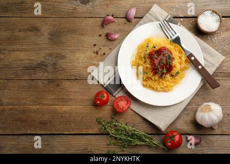 Leckerer Spaghetti-Kürbis mit Tomatensoße und Thymian, serviert auf einem Holztisch, flach liegend. Platz für Text Stockfoto