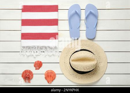 Strandtuch, Flip Flops, Strohhut und Muscheln auf weißem Holzhintergrund, flach gelegt Stockfoto