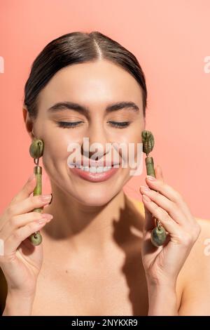 Eine nette Frau, die eine Gesichtsmassage mit Jade-Rollen machte, isoliert auf rosa, Stock Image Stockfoto