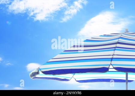 Offener großer gestreifter Strandschirm und wunderschöner blauer Himmel mit weißen Wolken im Hintergrund Stockfoto