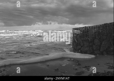 Gabionenkorb mit Steinen an einem Strand in Walton am Naze in Essex. Kalt, Winter, windiger Tag. Wellen schlagen gegen den Gabionenkorb. Stockfoto