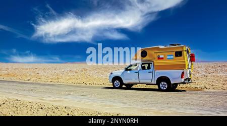 Einsamer Camper-Van auf einer Schotterstraße in der weißen, salzfarbenen Wüste, blauer Himmel - Salar de Atacama, Chile Stockfoto
