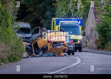 Box, Wiltshire, UK, August 4. 2022, ein orangefarbener Kia auf seinem Dach, nachdem er in einen Verkehrsunfall verwickelt war. Ein Krankenwagen ist auf der Straße sichtbar Stockfoto