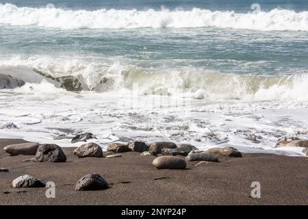 Wellen stürzen zwischen den verstreuten Kieseln am Strand von Ajuy, Fuerteventura. Stockfoto