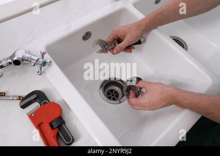 Professioneller Klempner, der den Wasserhahn in der Küche repariert, über der Aussicht Stockfoto