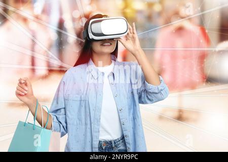 Junge Frau mit Einkaufstaschen, die ein Virtual-Reality-Headset in einem simulierten Geschäft verwendet Stockfoto