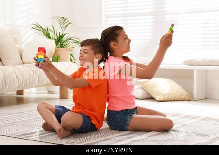 Kinder, die zu Hause mit Pop-IT-Spielzeugen spielen, bekommen Spielzeuge auf dem Boden Stockfoto