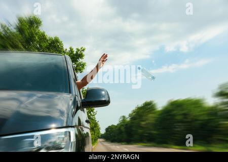 Der Fahrer wirft die Plastikflasche vom Autofenster weg. Müll auf der Straße Stockfoto