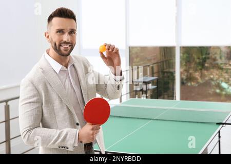 Geschäftsmann mit Tennisschläger und Ball in der Nähe des Tischtennistisches im Büro. Platz für Text Stockfoto