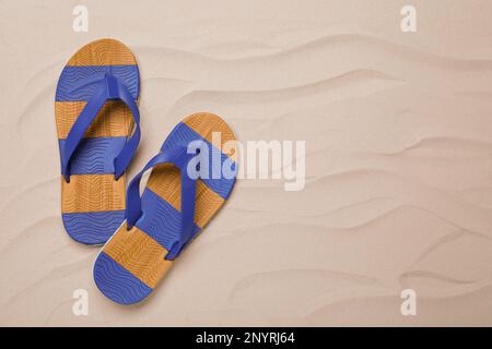 Ein Paar gestreifte Flip-Flops auf Sand, flach liegend. Platz für Text Stockfoto