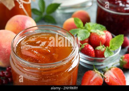 Gläser mit verschiedenen Marmeladen und frischem Obst auf dem Tisch, Nahaufnahme Stockfoto