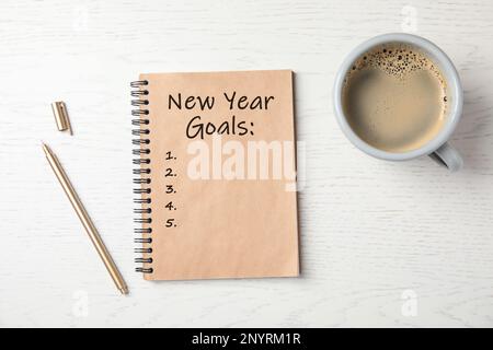 Notizbuch mit Aufschrift „Silvester-Ziele“, Tasse Kaffee und Stift auf weißem Holztisch, flach liegend Stockfoto