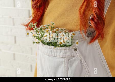 Eine Frau mit wunderschönen, zarten Kamillenblumen in der Tasche des weißen Overalls, Nahaufnahme Stockfoto