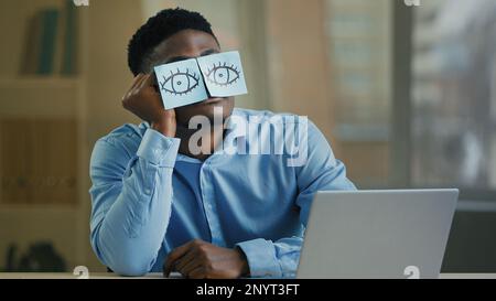 Verschlafener, fauler Büroangestellter, Geschäftsmann, afroamerikanischer Angehöriger, der an der Rezeption sitzt und ein Gesicht trägt, lustige komische Aufkleber, falsche Augen erschöpft Stockfoto