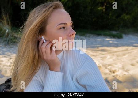 Glückliche junge Frau am Strand Meer Meer. Tragen von kabellosen Kopfhörern, die eine Audio-Heilklang-Therapie durchführen, während Sie sich der Natur bewusst sind. Wohlbefinden Einheit mit Natur Gesundheit Achtsamkeit. Genießen Sie Entspannung im Freien Stockfoto