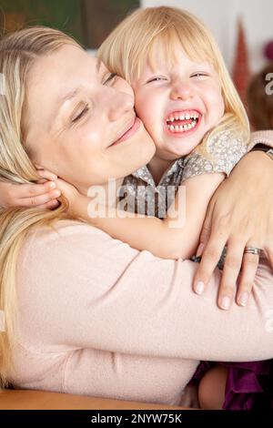 Familienleben, Große Umarmungen. Ein aufrichtiger Moment bedingungsloser Liebe zwischen einer jungen Mutter und ihrer jungen, aufgeregten Tochter. Aus einer Reihe von zugehörigen Bildern. Stockfoto