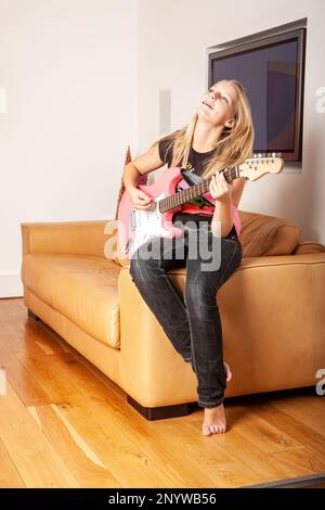 Familienleben, Pink Electric Guitar. Eine junge Gitarrenspielerin, die mit ihrem Instrument posiert. Aus einer Reihe von zugehörigen Bildern. Stockfoto