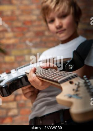 Familienleben, Junger Gitarrist. Ein abstrakter Winkel am Hals einer elektrischen Gitarre, der von einem Jungen gehalten wird. Aus einer Reihe von zugehörigen Bildern. Stockfoto