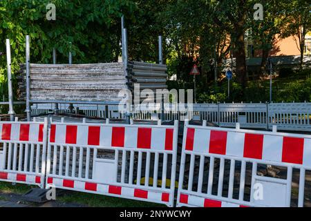 Auf dem Fußgängerbelag der Straße steht eine große Gruppe von weißen und roten Kunststoffbarrieren. Gerüste im Hintergrund gestapelt. Stockfoto