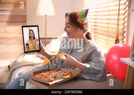 Eine Frau mit einem Stück Pizza hat eine Online-Party über Tablet zu Hause während Quarantäne-Lockdown Stockfoto