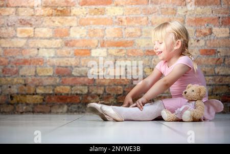 Familienleben, Kleine Ballerina. Ein junges Mädchen, das seine ersten Ballettzüge mit etwas Hilfe von Teddy übt. Aus einer Reihe von zugehörigen Bildern. Stockfoto