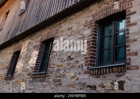 Eine Reihe von Fenstern in der Wand eines alten Gebäudes aus gebrochenem Stein. Oberstes Stockwerk aus Holz. Stockfoto