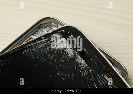 Kaputtes Smartphone auf hellem beigefarbenem Holzhintergrund, Nahaufnahme. Gerätereparatur Stockfoto