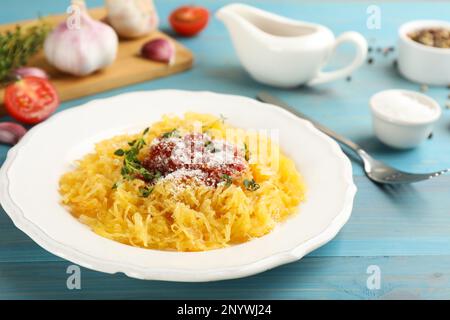 Leckerer Spaghetti-Kürbis mit Tomatensoße, Käse und Thymian auf einem hellblauen Holztisch Stockfoto