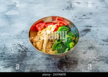 Ein gebratener Hähnchensalat mit Käse, gewürfelte Tomaten, gewürfelter Brokkoli, gekochte Quinoa, Spinatblätter in einer Edelstahlschüssel Stockfoto