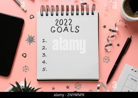 Aufschrift 2022 Tore im Notizbuch und verschiedene Objekte auf pinkfarbenem Hintergrund, flach liegend. Neujahrsziele Stockfoto