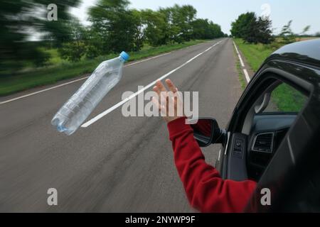 Der Fahrer wirft die Plastikflasche vom Autofenster weg. Müll auf der Straße Stockfoto