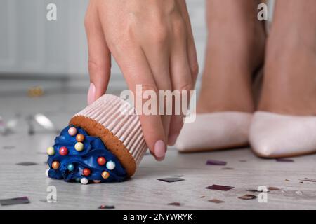 Eine Frau, die einen heruntergefallenen Cupcake vom Boden abholt, macht Schluss. Probleme passieren Stockfoto