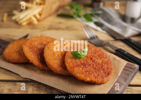 Köstliche gebratene panierte Schnitzel mit Basilikum auf einem Holztisch Stockfoto