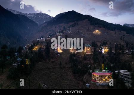 Drohnenlandung aus der Luft mit beleuchteten mehrstöckigen Gebäuden am Abend auf der Seite des Hügels, wobei die Einkaufsviertel der Hotels in manali, shimla, gezeigt werden Stockfoto