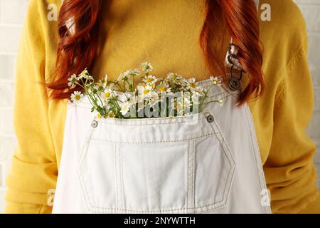 Eine Frau mit wunderschönen, zarten Kamillenblumen in der Tasche des weißen Overalls, Nahaufnahme Stockfoto