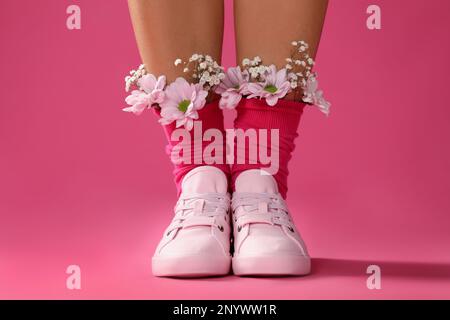 Frau mit wunderschönen zarten Blumen in Socken auf pinkfarbenem Hintergrund, Nahaufnahme Stockfoto