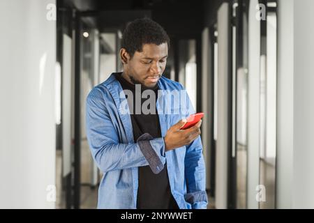 Afroamerikaner, seriöser Mann, der rotes Handy im Bürogebäude benutzt, Internet, Breitband, 5G. Porträt eines nachdenklichen afroamerikaners im Amt Stockfoto