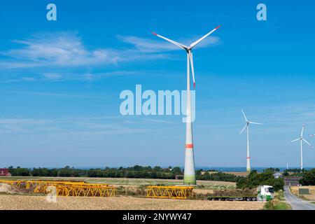 Gelbe Metallkonstruktionen auf dem Feld vor Windmühlen. In der Nähe ist ein Lastwagen. Stockfoto