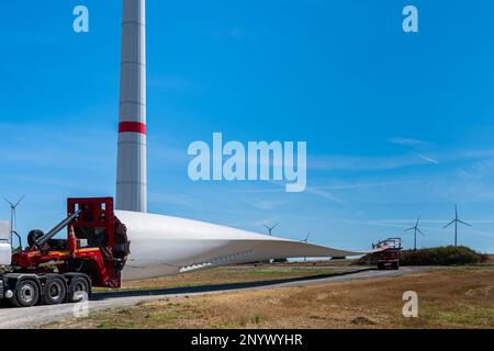 LKW mit einem Anhänger, beladen mit einem großen Windmühlen-Propeller. Steht auf einer Landstraße vor der Kulisse von Windmühlen. Stockfoto