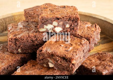 Eine Charge frisch gebackener dreifach-Schokoladen-Brownies auf einer Holzplatte. Die Brownies sind noch warm und klebrig. Ein Genuss Stockfoto