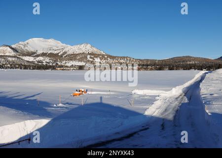 Die Sherwin Creek Road erstreckt sich durch Schneefelder in Richtung Mammoth Lakes mit dem Skigebiet Mammoth Mountain im Hintergrund. Stockfoto