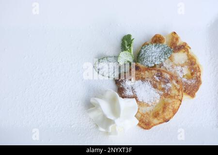 Pfannkuchen auf weißem rechteckigem Teller mit Minzeblättern und Puderzucker verteilt Servieren Dessert gesundes Essen Pfannkuchen mit Äpfeln Beeren Mittagessen Oma's Küche für Kinder Stockfoto