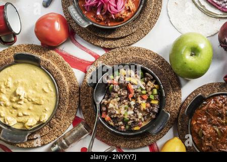 Auswahl an Gerichten mit mexikanischen Rezepten, mexikanischem Ropa vieja Eintopf mit Saucen, Kürbisblumeneintopf und frischem Obst Stockfoto