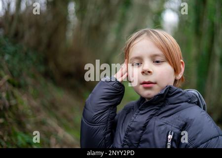 Junger Junge in der freien Natur. Ein Junge von acht zehn Jahren in einer warmen Jacke im Wald. Kindische Zweifel, Reflexionskonzept. Stockfoto