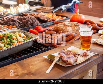 Ein Haufen leckeres Essen auf einem Jahrmarkt, Festival, Street Food Stand, viele verschiedene Gerichte und eine Tasse Bier, niemand. Catering, Restaurants im Freien Stockfoto