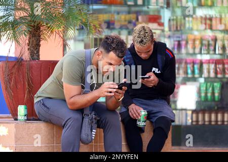 Zwei Typen sitzen mit Smartphones auf einer Straße. Online-Kommunikation im Freien Stockfoto